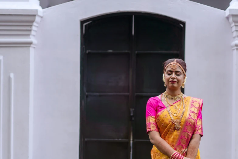 an indian woman in a traditional yellow dress standing next to black doors