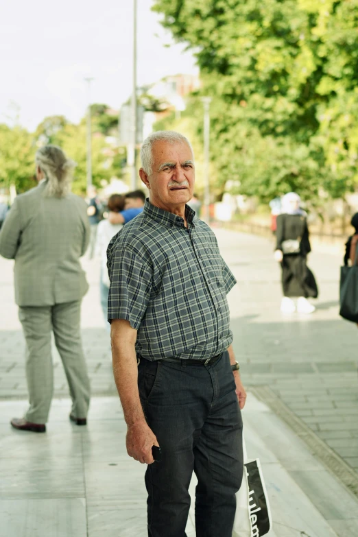 an older man is standing on a sidewalk while a woman walks by