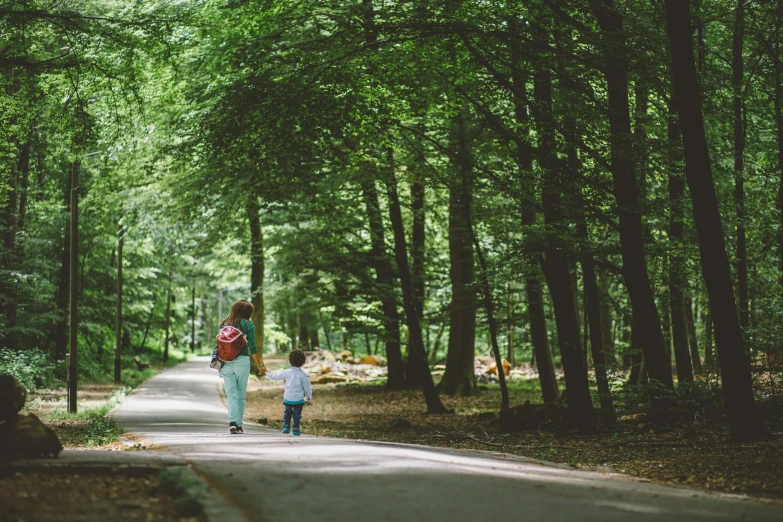 woman and child walking down tree lined country lane in park