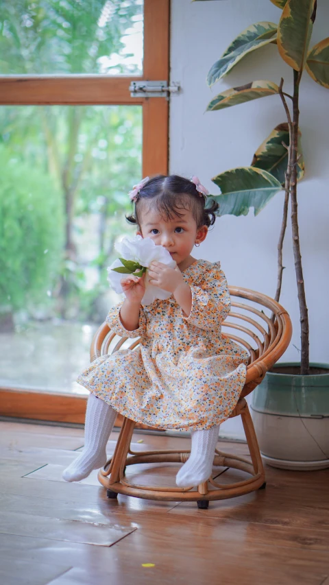 a girl in flowered dress sitting on a wooden chair