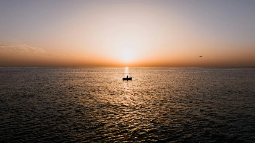 the sun sets behind the boat in the middle of the water