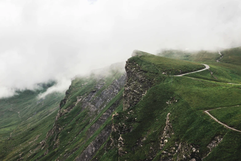 a cliff edge with green grass and rock, has several winding ridges