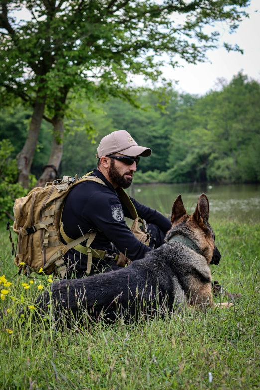 the man is relaxing in the grass with his german shepard