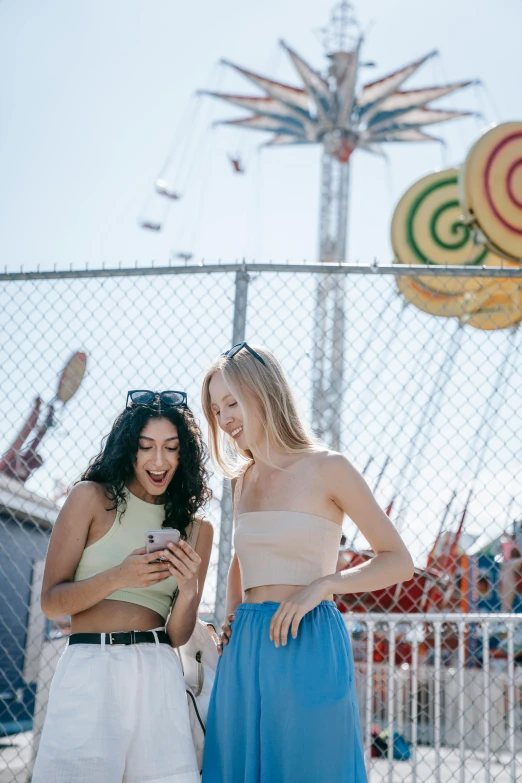 two pretty women standing next to each other near a fence