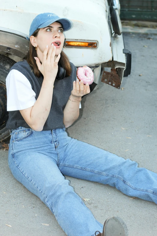 woman sitting on ground eating donut sitting next to car