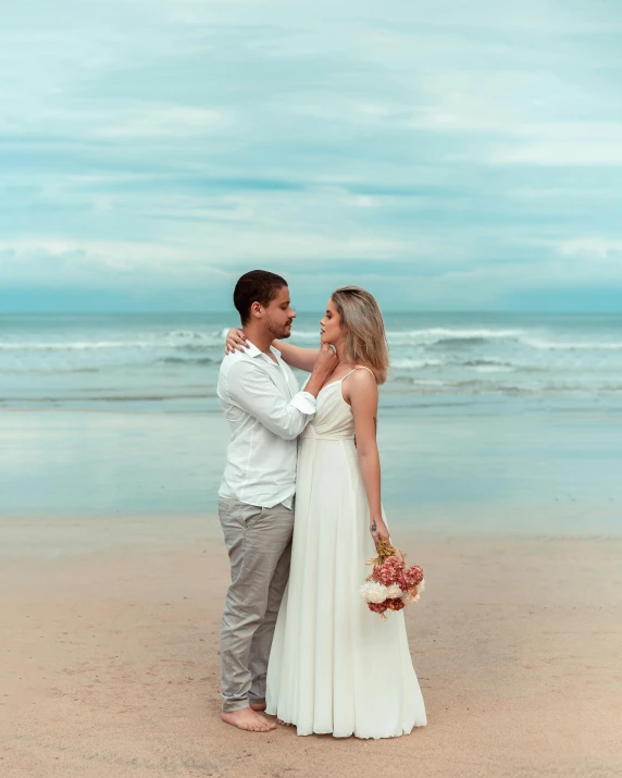 a man in a white shirt and woman in a white dress standing on the beach