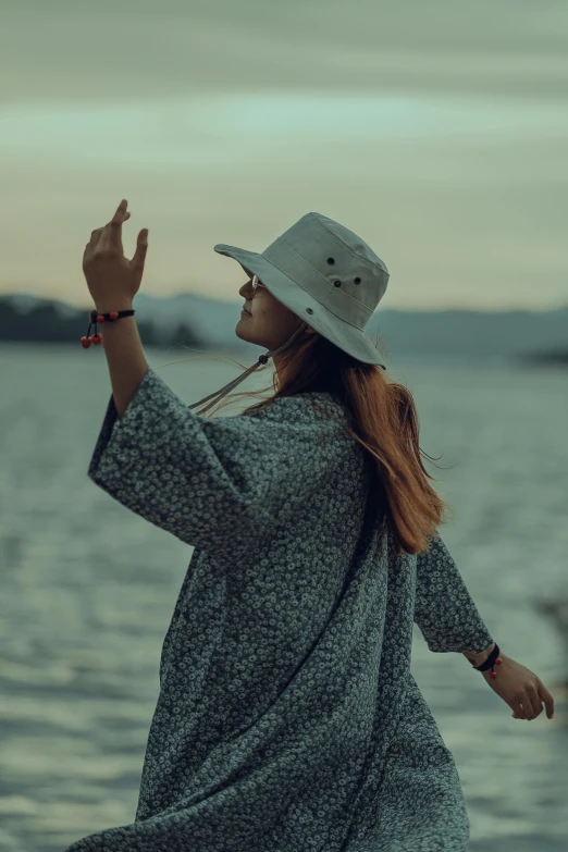 a woman with long hair and a hat on is by the water