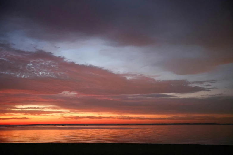 a beach view at sunset with a few clouds in the sky