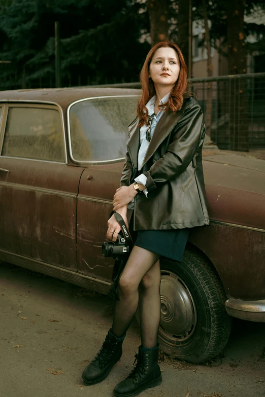 the red - haired woman with black stockings is leaning on the car door