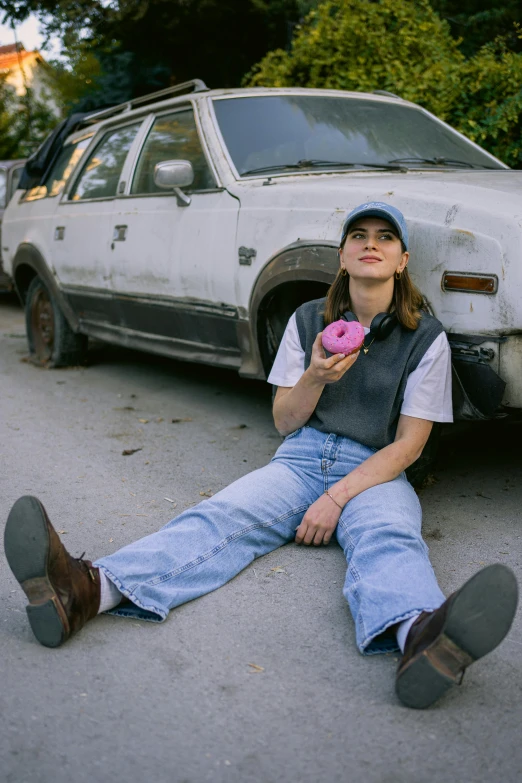 the woman is eating a doughnut while laying next to a parked car