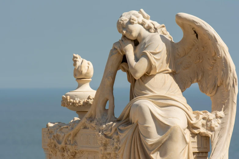 an angel sculpture near the ocean, holding a globe