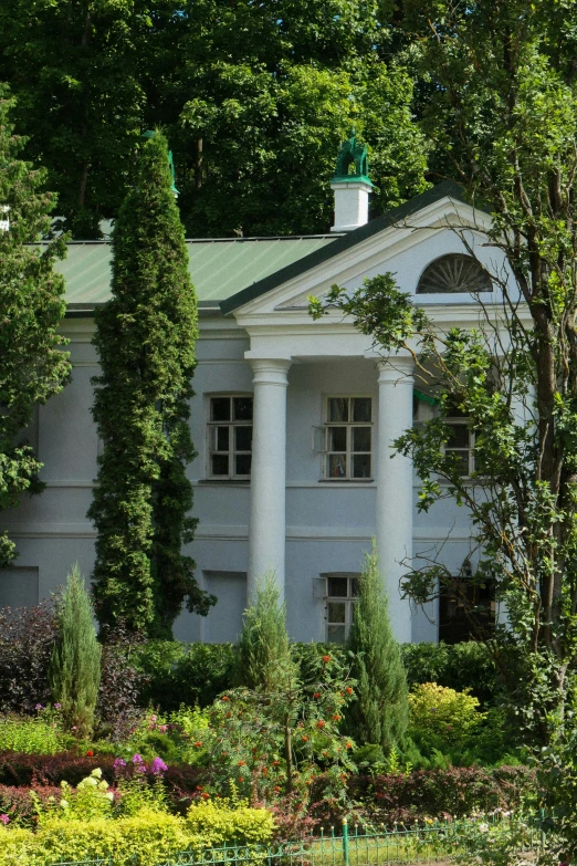 an old, white house is surrounded by green trees and flowers