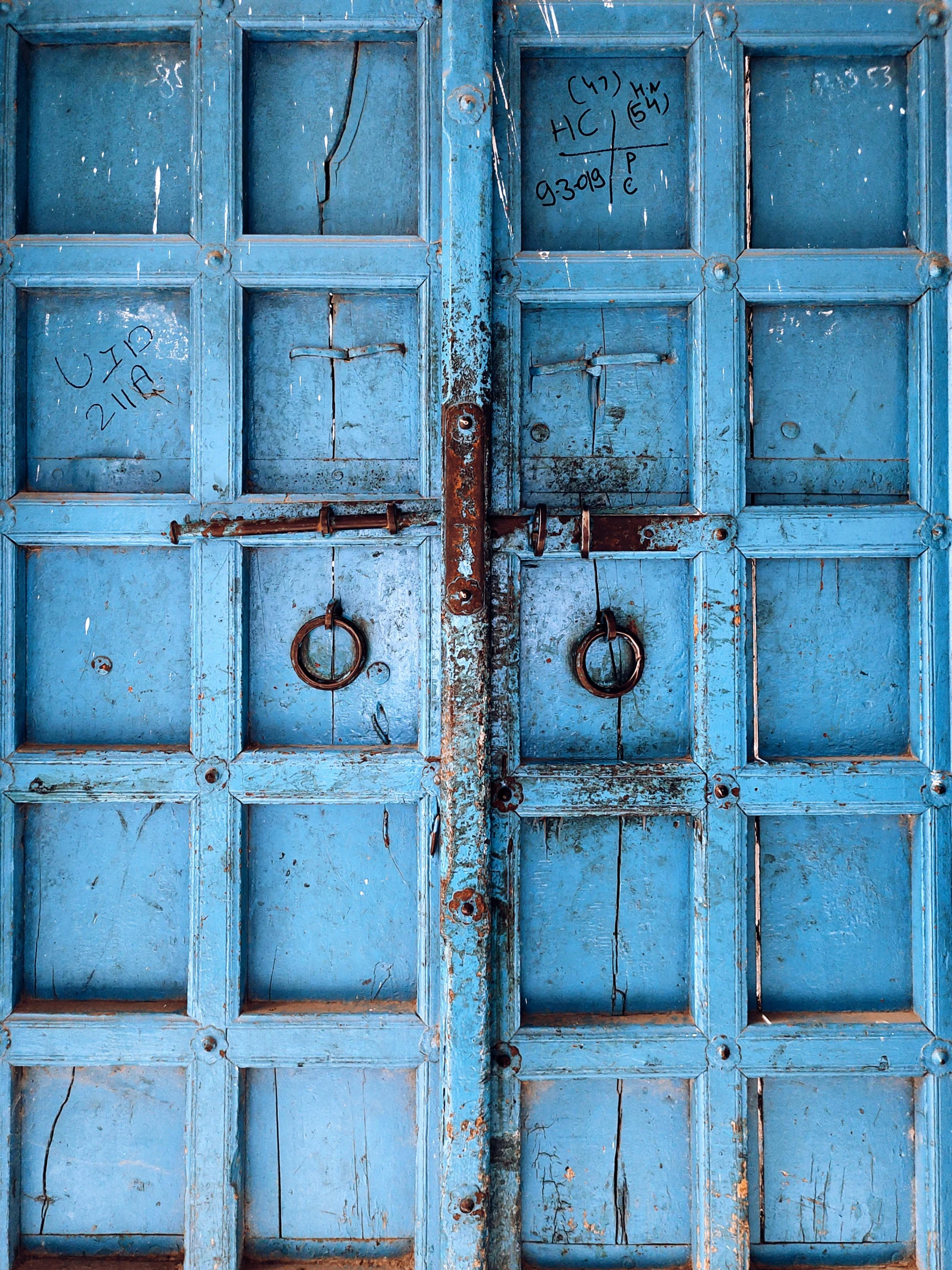 a blue door with a metal knockle and rusty handles