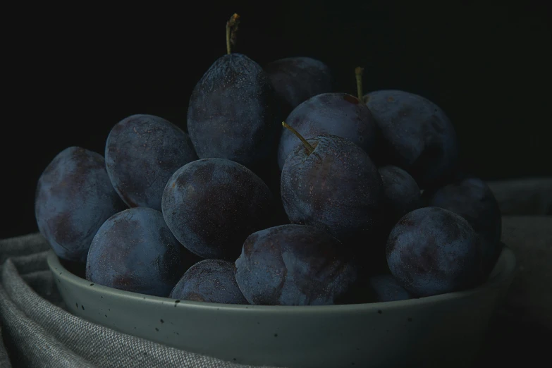 bowl filled with lots of plums sitting next to a piece of fabric