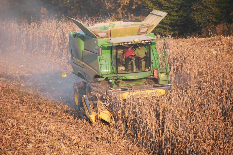 a tractor is driving in a field and people are standing on the back