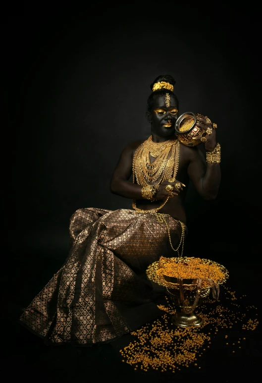 a woman dressed in gold is seated on a stool