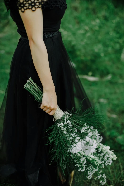 the hand that is holding a bouquet of flowers is in front of a woman in a black dress