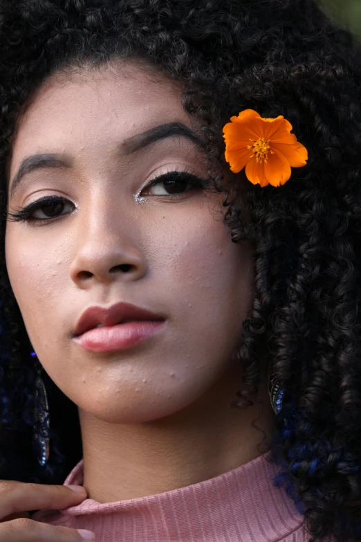 a young woman with long black curly hair and bright orange flower in her hair