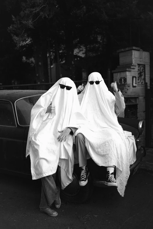 two people sitting on a car dressed in white and covering them with scarves