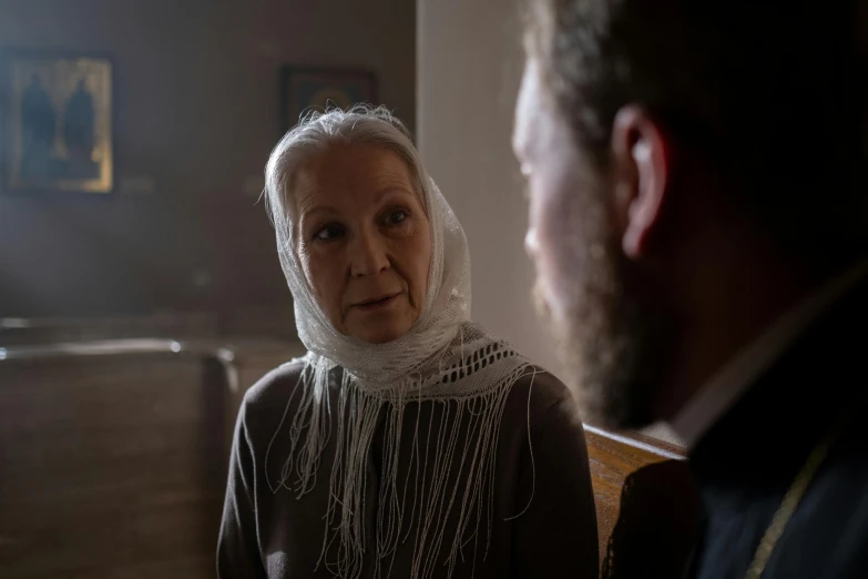 an older woman with a white scarf on her head standing near a man in black