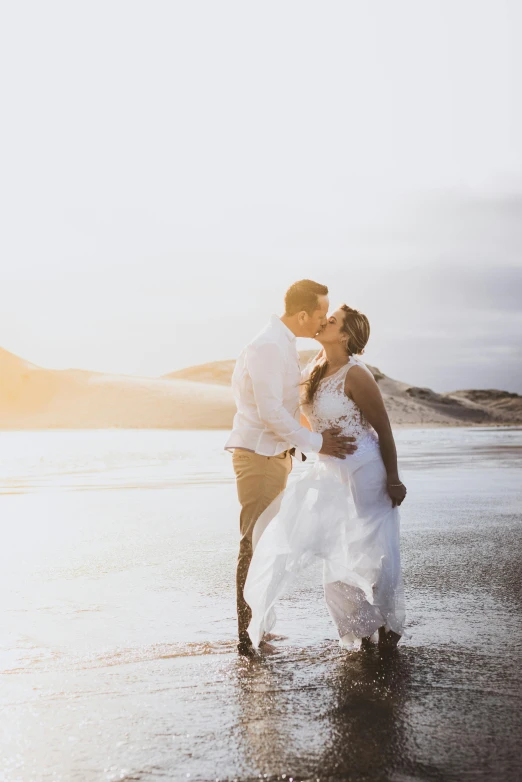 a couple in white walking on a beach at sunset