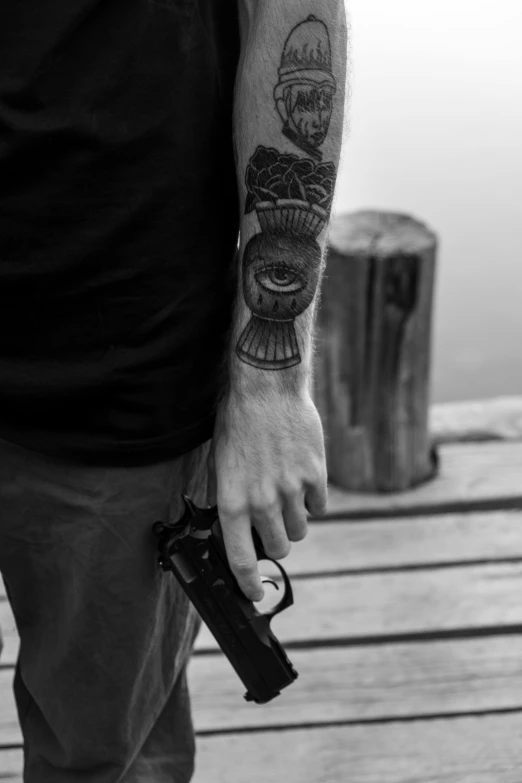 a tattooed man holding a gun and pointing at soing in front of him