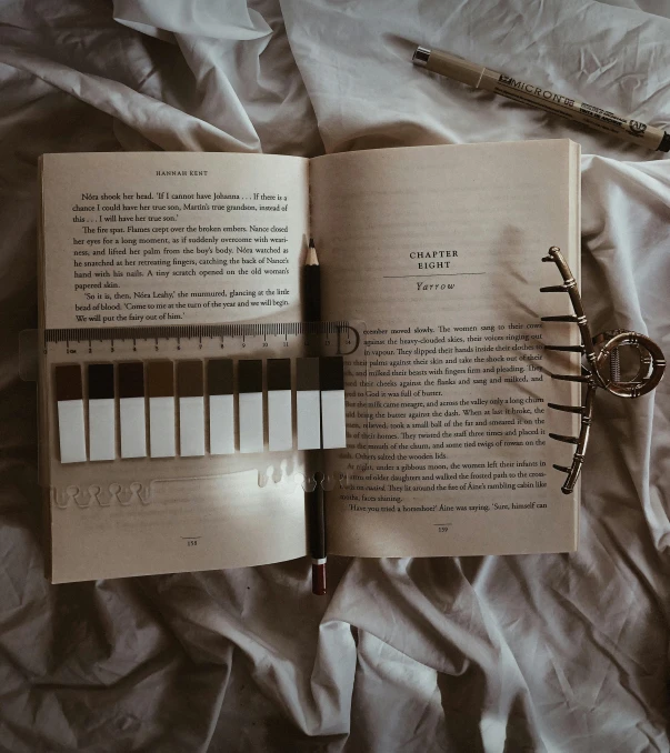 an open book next to a pair of scissors and a pen on top of a bed