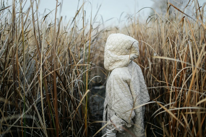 the child in a white jacket stands in tall grass