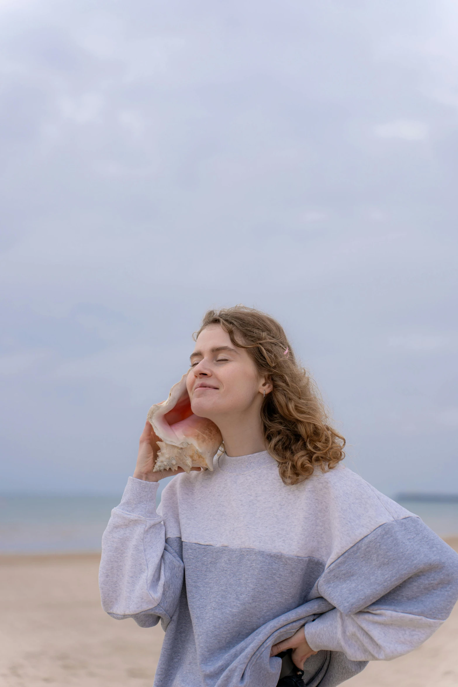 a  in a gray sweater looks off at the beach