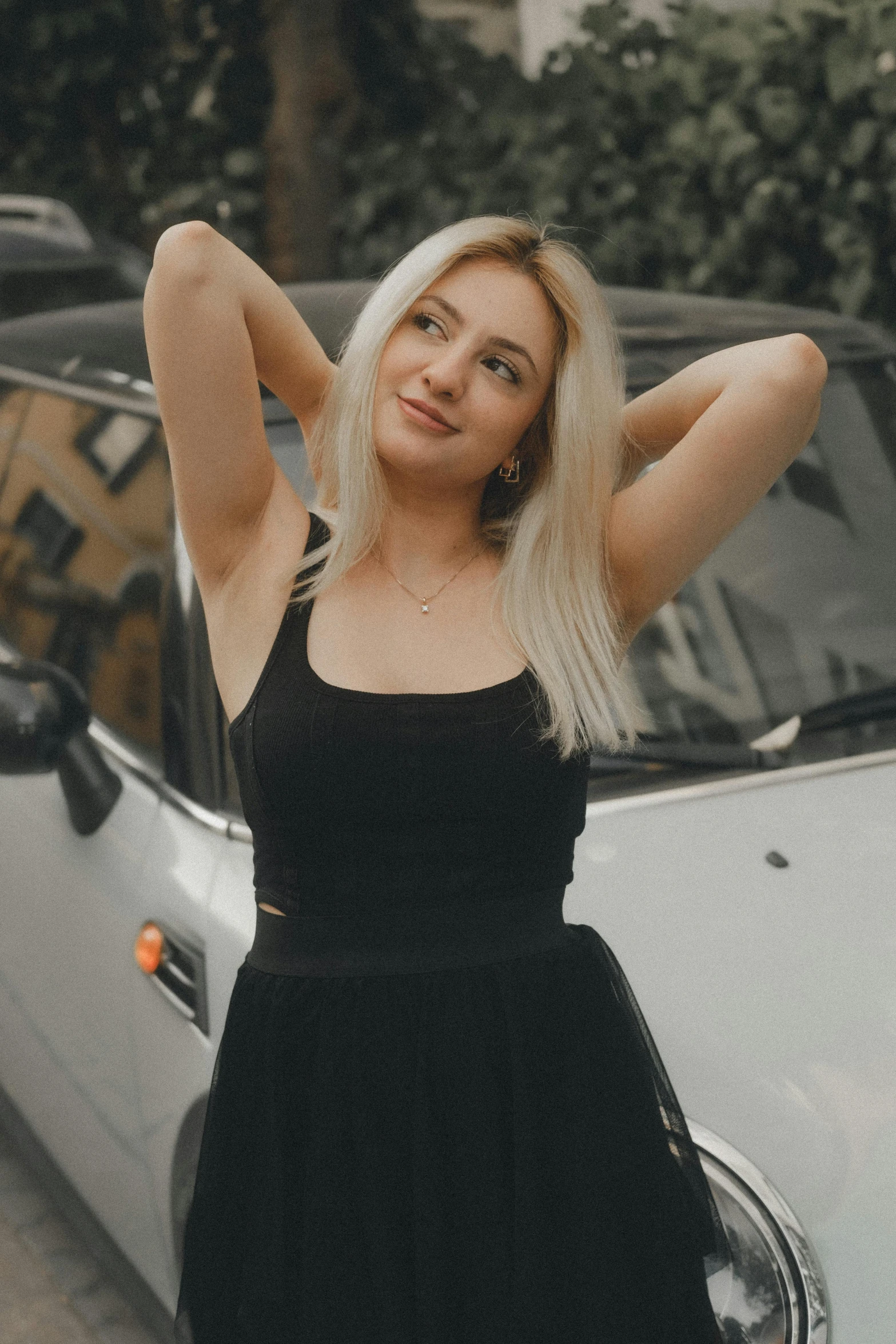 a woman in a short black dress posing next to a parked car