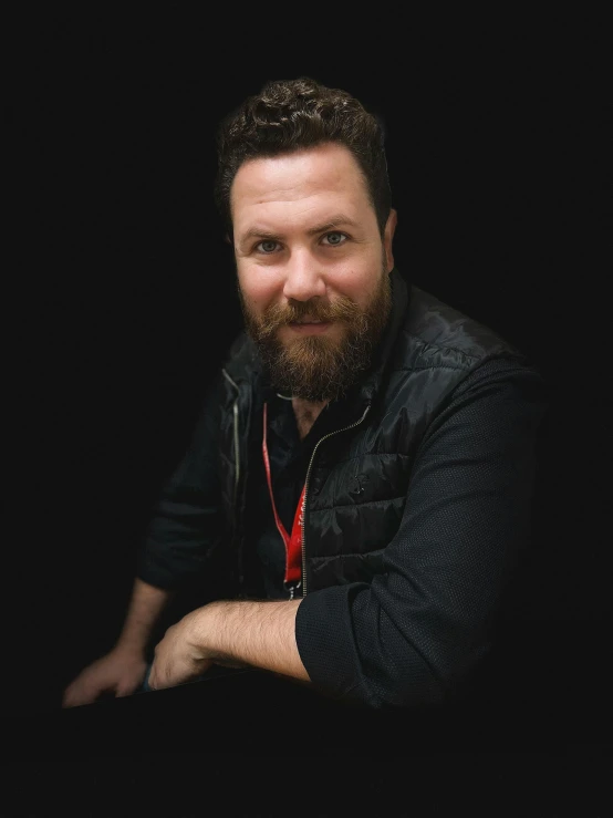 a bearded man in black sweater and beard with a camera around his neck