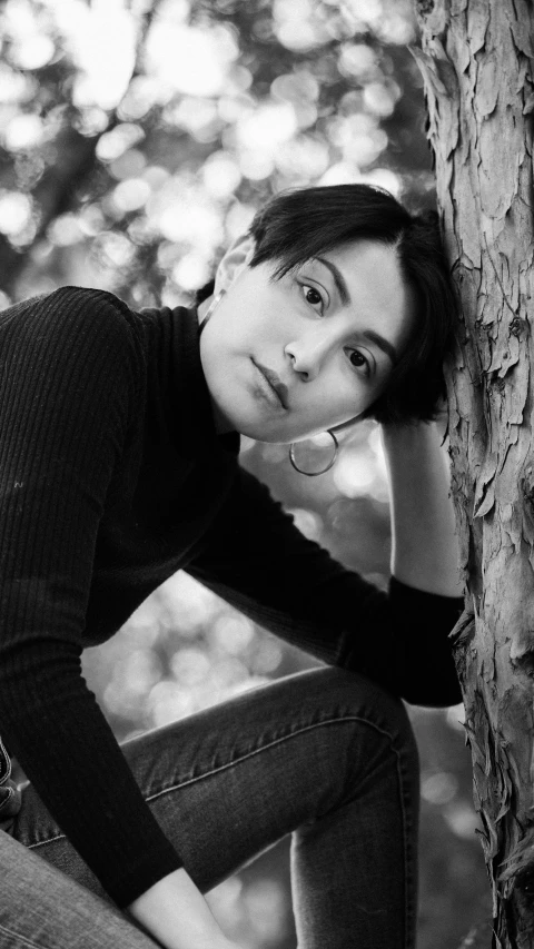 a young woman is posing near the tree