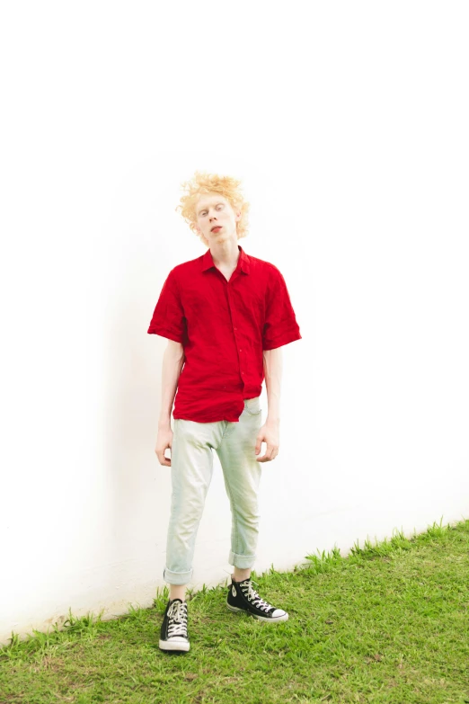 a man in a red shirt leaning against a white wall