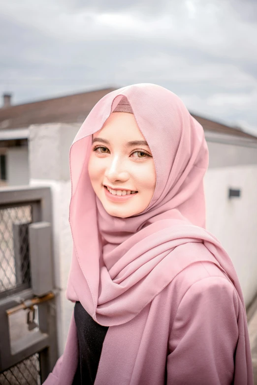 a woman wearing a pink head scarf stands in front of a fence