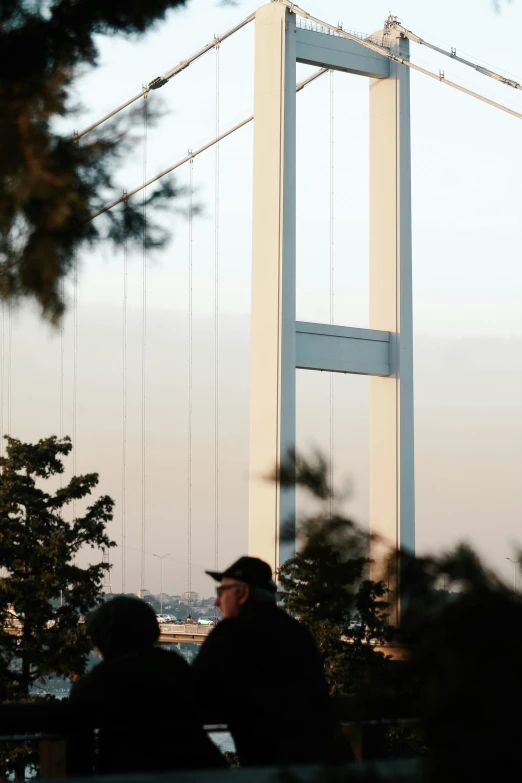 two men sitting on the bench outside a large bridge