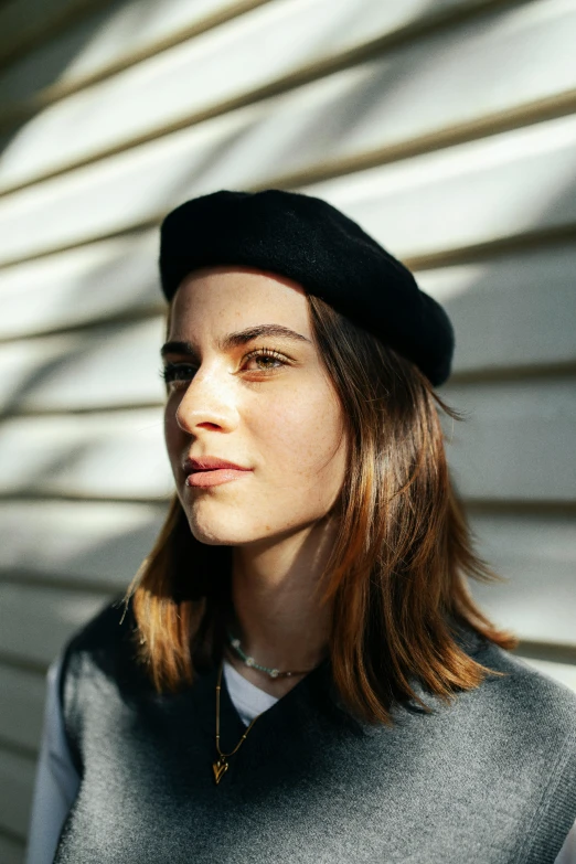 a girl wearing a black beret and standing against a white wall