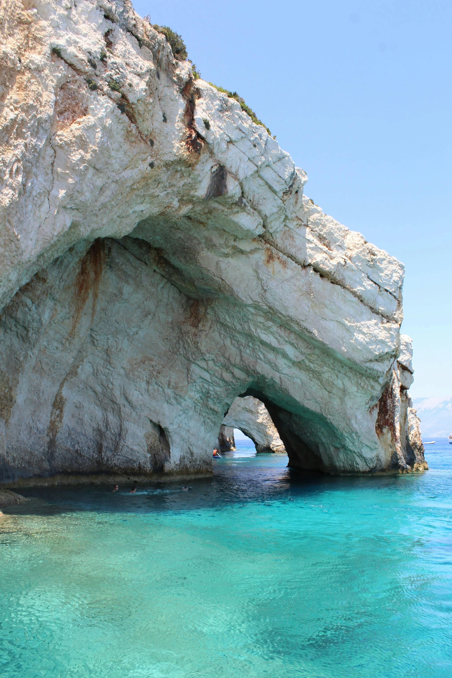 a rocky island with large doorways next to blue water