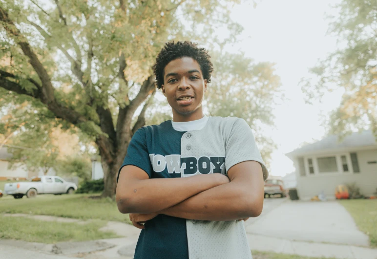 a young man poses with his arms crossed outside