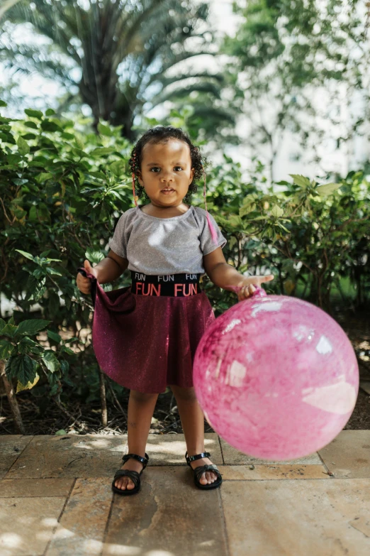 little girl in grey t - shirt holding up a pink ball