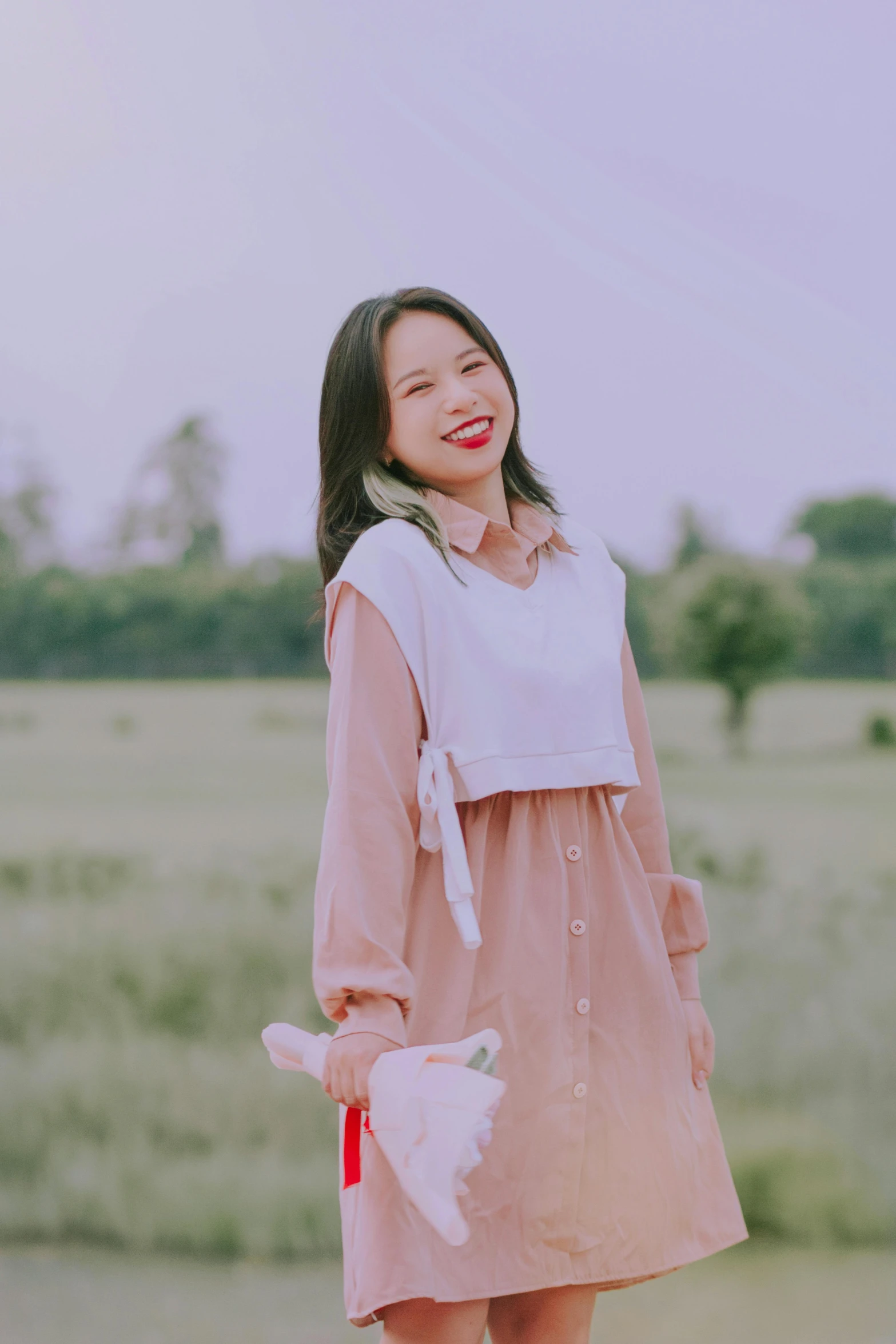 an asian woman with short black hair and a pink dress smiles in a field
