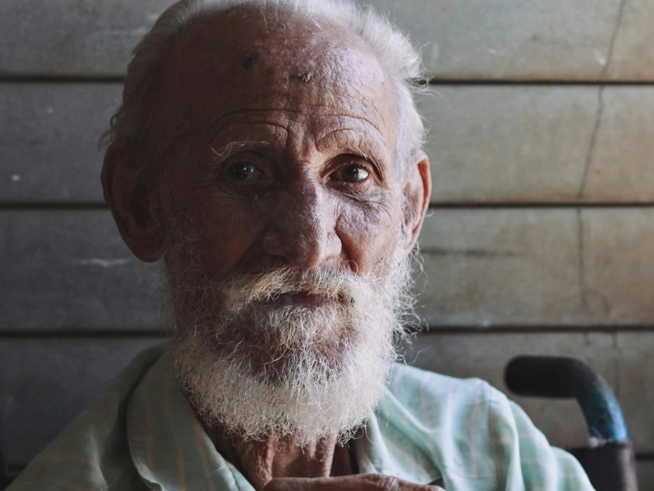 an old man with a long white beard sits by a wall