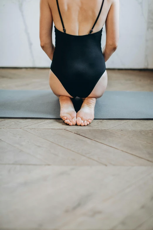 a young woman sits on the floor in her swimsuit and bends over to practice yoga