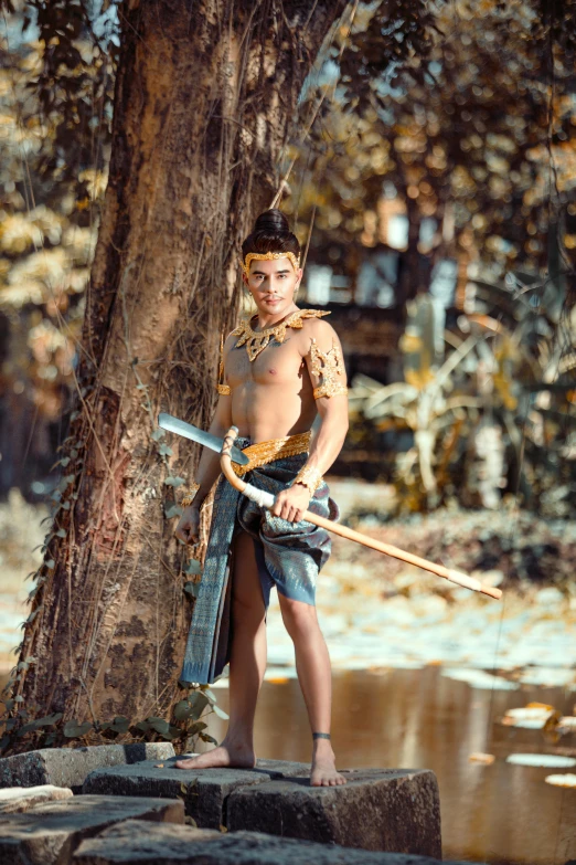 a  in a native indian style costume poses by a tree