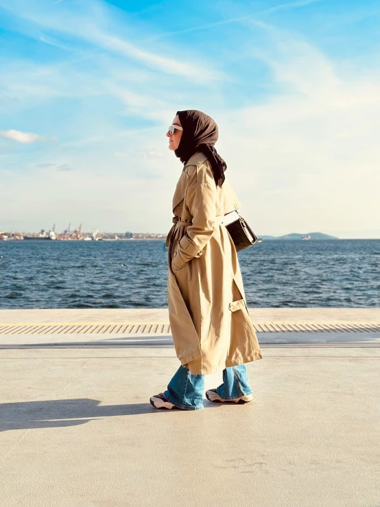 woman wearing trench coat standing on sidewalk by ocean