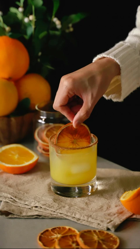 a person is putting an orange slice into a small glass