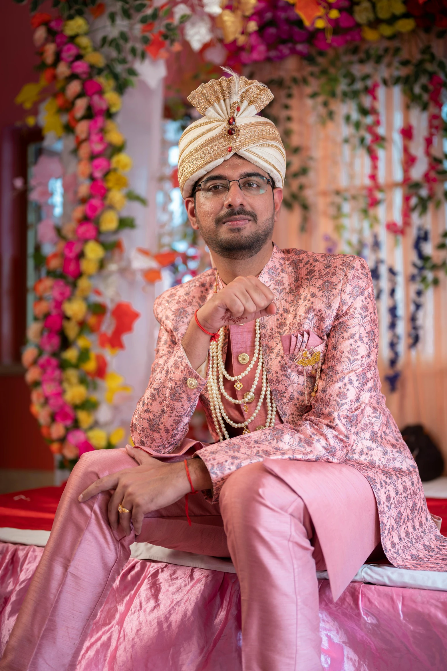 man dressed in pink attire sitting down with beaded necklaces