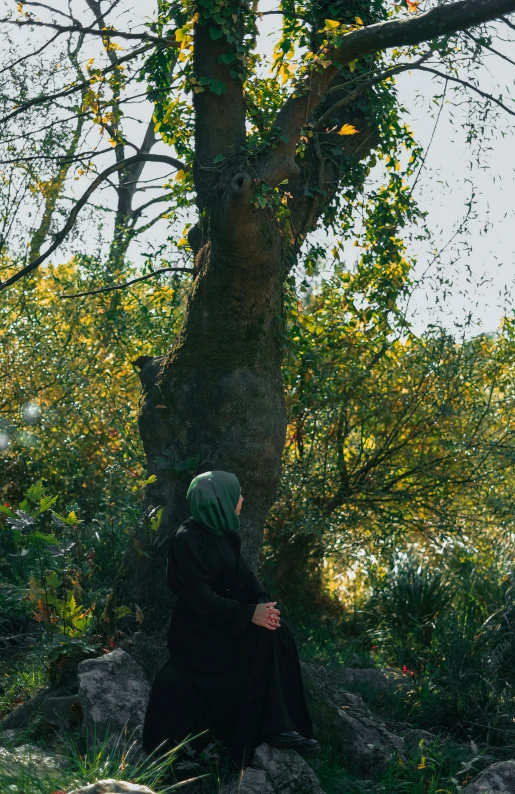 a person with a shawl sits on a hill and looks into the distance