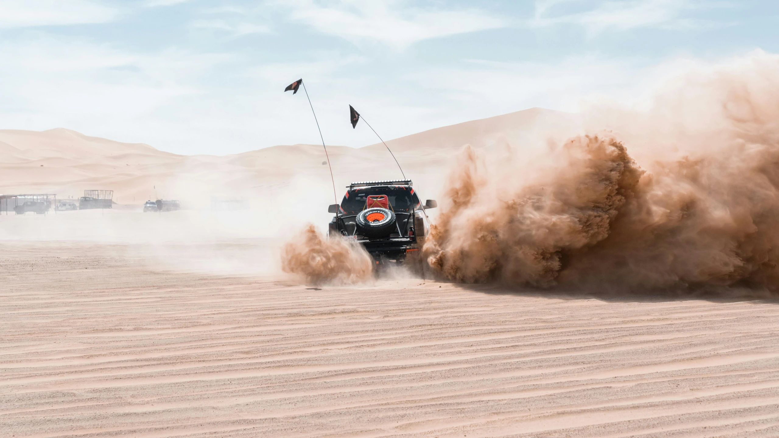 two vehicles drive through the desert with dust