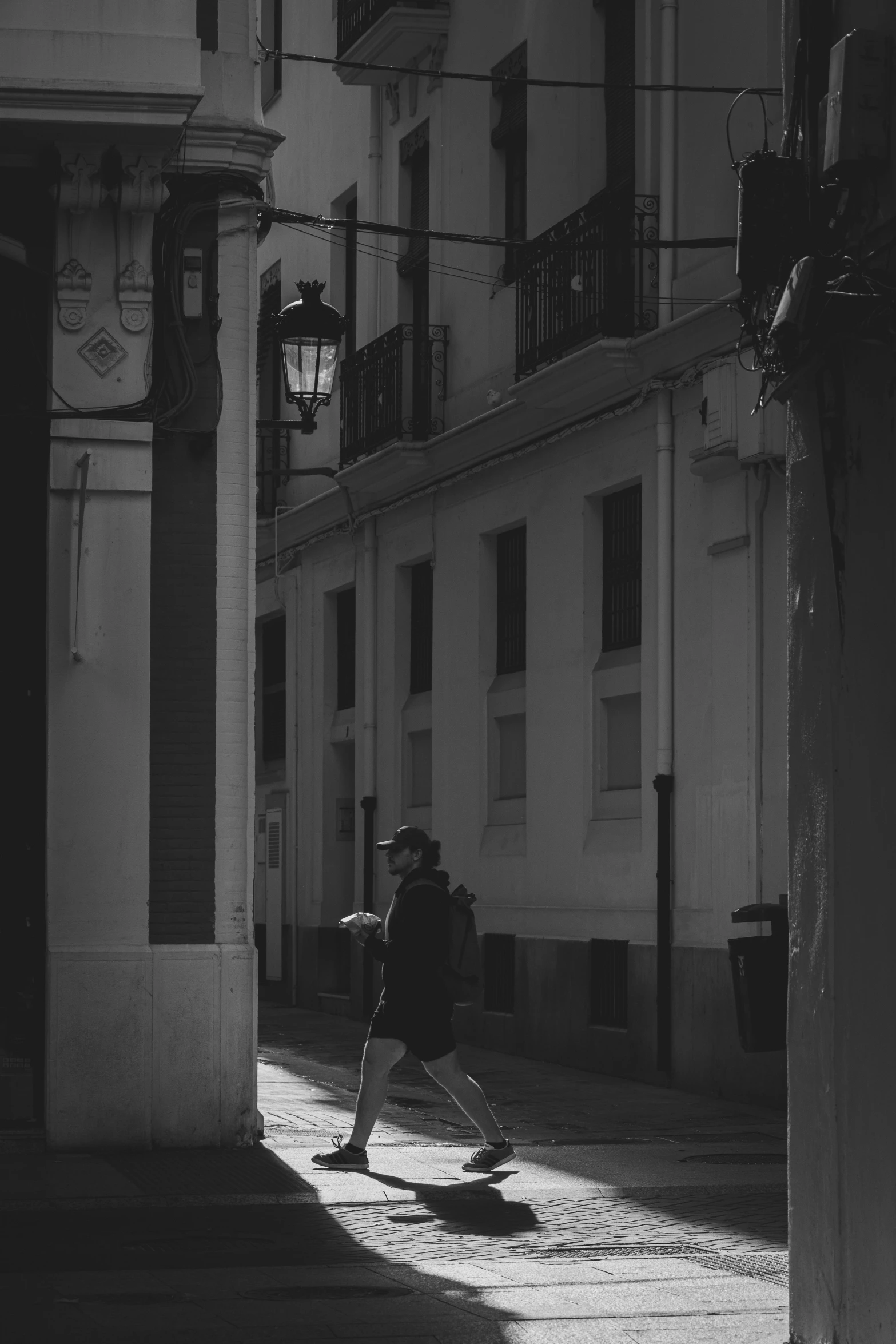 the person has a back pack in the shadows of some building