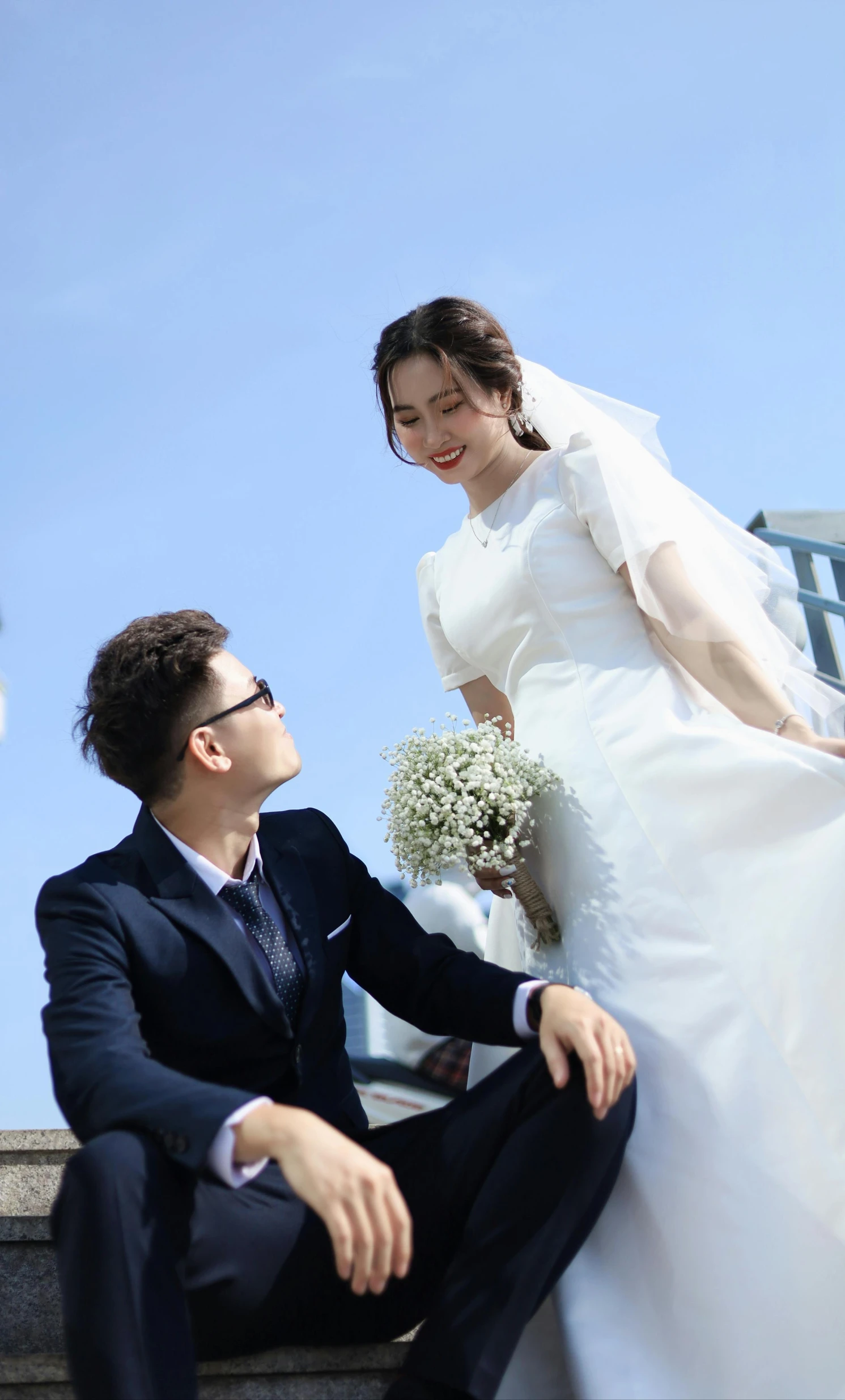 a young man in a suit sitting next to a young woman dressed in a white wedding dress